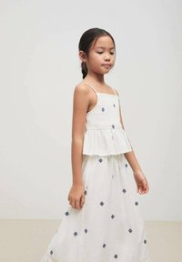 Robe blanche sans manches avec ourlet volanté et broderie en forme de diamant bleu, fabriquée en tissu léger, dotée d'un corsage ajusté et d'une jupe évasée.