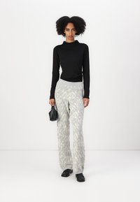 Black ribbed long-sleeve top paired with textured gray patterned wide-leg pants, complemented by a small black handbag and black shoes.