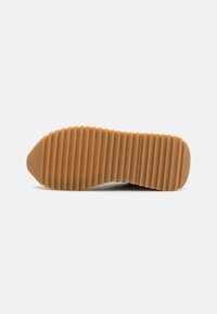 Semelle de chaussure présentant un design nervuré, en caoutchouc de couleur beige, avec un bout arrondi et une surface texturée pour une meilleure adhérence.