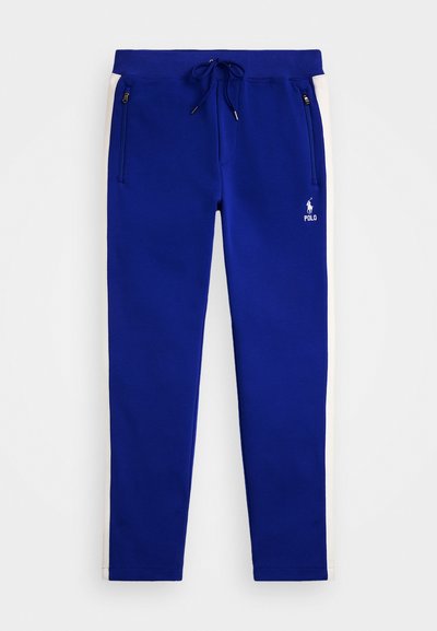 Calças de jogging azuis feitas de um tecido com uma textura suave, apresentando riscas laterais brancas, cintura elástica com cordão e bolsos com fecho éclair.
