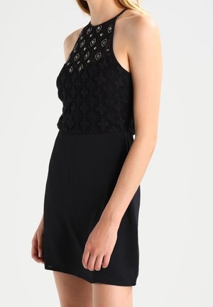 Robe noire avec un corsage texturé et à motifs agrémenté de embellissements, et une jupe lisse et fluide. Encolure halter et silhouette cintrée.