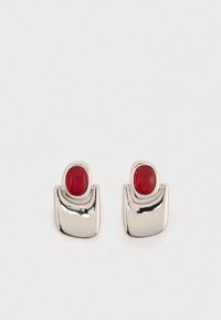 Srebrne naušnice s glatkim, zakrivljenim dizajnom imaju centriranu crvenu kamen. Ova kombinacija stvara moderan, minimalistički izgled.