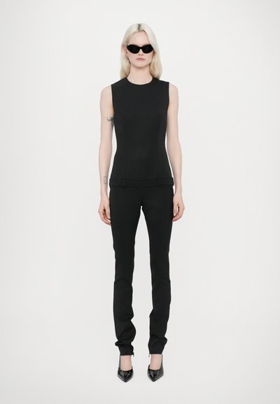 Haut sans manches noir et pantalon noir ajusté, tissu lisse, silhouette élégante, associé à des talons aiguilles noirs et des lunettes de soleil angulaires.