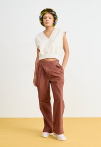 Beige ärmlös crop-top med V-ringning, parat med löst sittande byxor i rostfärg med knappförsedd midja och subtilt Nike-logotyp. Vita sneakers.