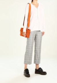 Ljusrosa långärmad topp med dragkedja, grå rutig croppade byxor, orange mocka axelväska, svarta plattformsskor med snörning.