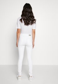 Weiße enge Jeans mit hoher Taille und Gesäßtaschen. Kombiniert mit einem schlichten weißen T-Shirt und weißen Sneakers. Glatter, dehnbarer Stoff.