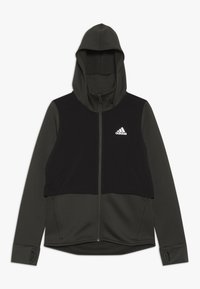Huppari tumman vihreänä ja mustana, jossa on karkea kangas, sile�ät paneelit, istuva huppu ja valkoinen Adidas-logo rintalla.