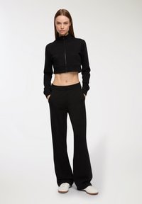 Giacca nera cropped con zip e colletto alto, abbinata a pantaloni larghi neri. Tessuto morbido e design informale.