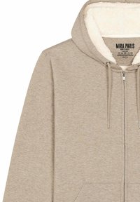 Felpa color beige con zip e rivestimento interno morbido e bianco. Presenta una tasca frontale e un cappuccio regolabile con cordini. Tessuto soffice e vestibilità comoda.