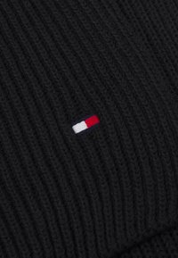 Beanie negru cu model rib ce include un mic logo cu accente roșu, alb și albastru. Textură moale, design ajustat, potrivit pentru vreme rece.
