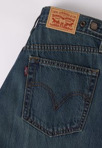 Πίσω τσέπη μπλε τζιν Levi's με χαρακτηριστική καρβουνωτή ραφή και δερμάτινη ετικέτα με το λογότυπο Levi Strauss & Co. στη μέση.
