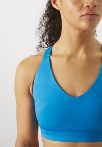 Μπλε αθλητικό σουτιέν με σχέδιο βαθούλου V, χωρίς ραφές και εφαρμοστή σιλουέτα, κατασκευασμένο από ελαστικό, αναπνεύσιμο ύφασμα.