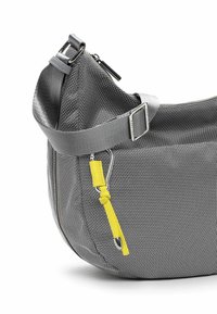 Grau gewebte Stofftasche mit gebogener Form, ausgestattet mit einem grauen Riemen und gelben Akzenten. Enthält ein Reißverschlussfach und metallische Beschläge.
