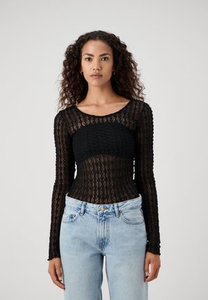 Svart langermet topp laget av teksturert blonde med rund hals, kombinert med lyse denimjeans som har en figursydd silhuett.
