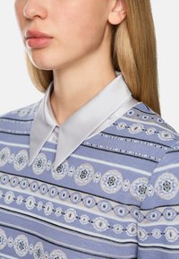 Light blue sweater featuring a subtle patterned design of circular motifs and striped accents, with a contrasting soft silver collar.