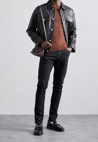 Svart läderjacka, rostfärgad tröja, mörka jeans, svarta loafers med guldaccenter och en liten crossbody-väska. Enkel, modern design.