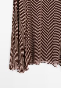 Jupe avec motif chevron marron et beige, tissu fluide avec légère translucidité et plis visibles à l'ourlet.