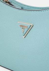 Světlomodrá texturovaná kabelka s trojúhelníkovým zlatým a modrým logem. Povrch má jemný ražený vzor a zipové zapínání.