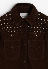 Camisa de ante marrón con detalles de tachuelas en los hombros, dos bolsillos delanteros y botones de metal negro, que ofrece una apariencia texturizada.