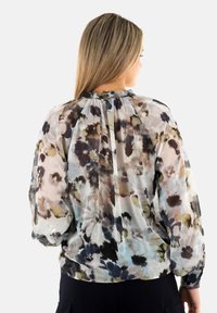 Blusa floral en tejido ligero y transparente con patrones multicolores. Detalle de pliegue en la parte trasera y escote fruncido. Mangas largas y abullonadas.