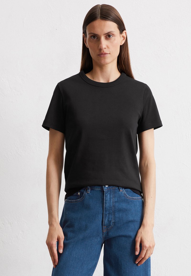 Zwarte katoenen t-shirt met korte mouwen, een ronde hals, en een losse pasvorm, gecombineerd met blauwe spijkerbroek. Gladde textuur, geen patronen.