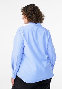 Light blue, long-sleeve shirt with vertical white stripes, buttoned cuffs, and a classic collar. Relaxed fit with a smooth texture.