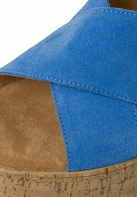 Sandale compensée en suède bleu avec des brides croisées, plateforme en liège et texture de semelle intérieure brune lisse. Détails de couture sur les brides.