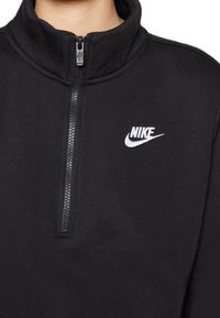 Svart Nike zip-tröja med hög krage, med en frontdragkedja och en vit Nike-logga broderad på vänster bröst.