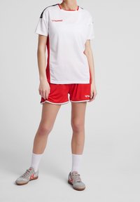 Conjunto deportivo rojo y blanco con una camiseta de manga corta y pantalones cortos a juego; la camiseta tiene detalles y un logotipo en negro; material ligero y transpirable.