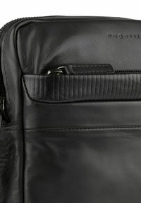 Schwarze Lederhandtasche mit einem Reißverschluss oben, strukturiertem Nähen und einer kleinen Vordertasche. Logo auf der Oberfläche geprägt. Glatte, feine Textur.