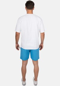 T-shirt bianco a maniche corte, pantaloni da bagno blu, e sneakers bianche. La t-shirt è semplice; i pantaloni sono di un blu uniforme con un dettaglio cucito.