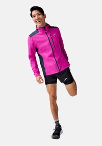 Bright pink running jacket with a navy back, featuring a zippered pocket and reflective accents, paired with black shorts and sneakers.