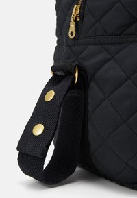 Borsa in tessuto trapuntato nero con hardware della cerniera dorato e una tracolla blu con bottoni a pressione per il fissaggio. Texture liscia con motivo distintivo.