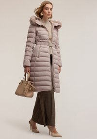 Světlofialový prošívaný kabát s kapucí s umělou kožešinou, s páskem v pase a zipovými kapsami. Kombinován se hnědou kostkovanou sukní a béžovými podpatky.