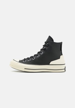 Zapatillas altas de cuero negro con punta redonda, suela de goma en color crema, con cordones negros y detalles laterales en negro.