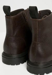 Botas de tobillo de cuero marrón con acabado texturizado, cremalleras laterales y suelas de goma negra. Presentan tiradores para facilitar su uso.