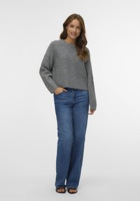 Maglione grigio a maglia corto con maniche lunghe abbinato a jeans larghi blu e sandali neri. Nota la texture a maglia piatta e la vestibilità ampia.