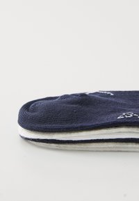 Calzini di cotone blu navy a trama a coste, piegati ordinatamente, che mostrano strisce bianche e grigie lungo i bordi. Decorati con motivi discreti.