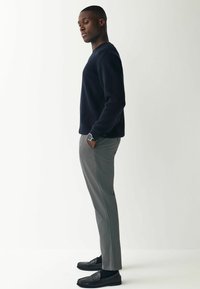 Mørkeblå crewneck sweater, grå skræddersyede bukser, sorte loafers. Glatte teksturer, simpelt design og kontrasterende farver.