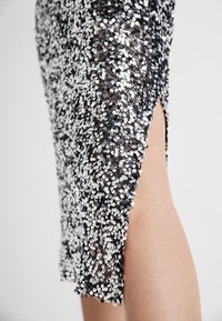 Črna in srebrna obleka s svitki z razporkom do stegna, ki se ponaša z oprijetim krojem in teksturirano površino zaradi prekrivajočih se svitkov.