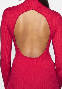 Red ribbed dress with a high neck and long sleeves, featuring a large open back design and smooth texture.