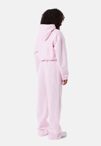 Conjunto de sudadera y pantalones de chándal en color rosa. Tejido suave, corte relajado, con capucha y bolsillos. Los pantalones tienen un detalle de costura blanca a lo largo de las costuras.