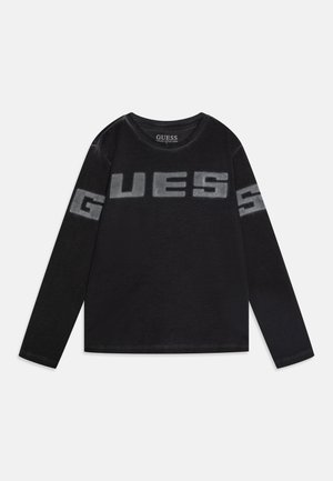 Chemise noire à manches longues avec "GUESS" imprimé en grandes lettres grises délavées sur la poitrine et les manches, col rond.