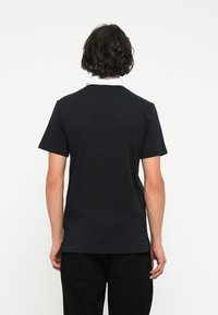 Tricou din bumbac negru cu guler alb, cu mâneci scurte și un design drept, prezentat din spate. Simplu și de culoare uniformă.