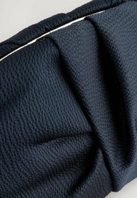 Sötétkék textil textúrált felülettel, redőkkel és finom fényű kivitelben. Vékony, kontrasztos szegéssel keretezve.