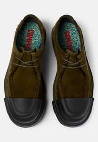 Scarpe in suede verde oliva con punta in gomma nera, lacci grigi e plantare decorato con macchie multicolori.