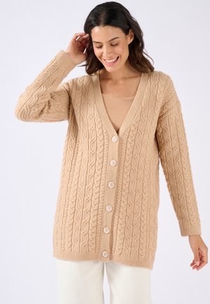 Gilet en tricot cable beige avec un décolleté en V, des manches longues et six boutons à l'avant. Tissu texturé avec une apparence douce.