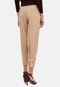 Beiga beskurna byxor med en slät textur, med sidofickor och knäppte ärmslut. Matchas med bruna högklackade sandaler.
