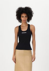 Melns ribots top ar izgriezumu, ar baltiem "PATRIZIA PEPE" uzrakstiem priekšā. Apvienots ar bēša taisnas griezuma svārkiem.