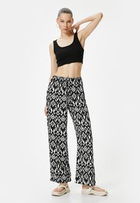 Mustat lyhyet topit, mustavalkoiset leveälahkeiset housut, joissa on kuvio, ja vaaleat alustakengät. Housuissa näkyvä geometrinen kuvio.